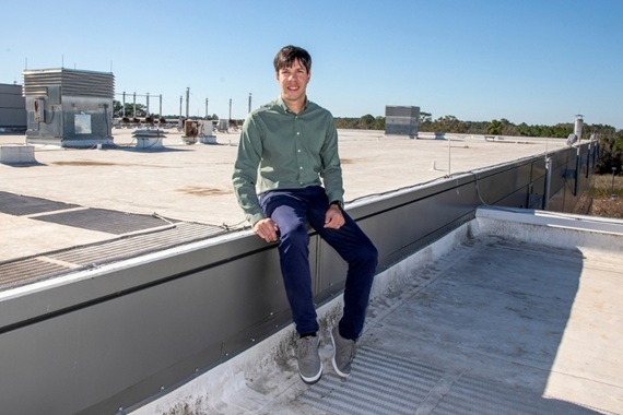A man sits on a wall on the flat roof of a low-rise building.